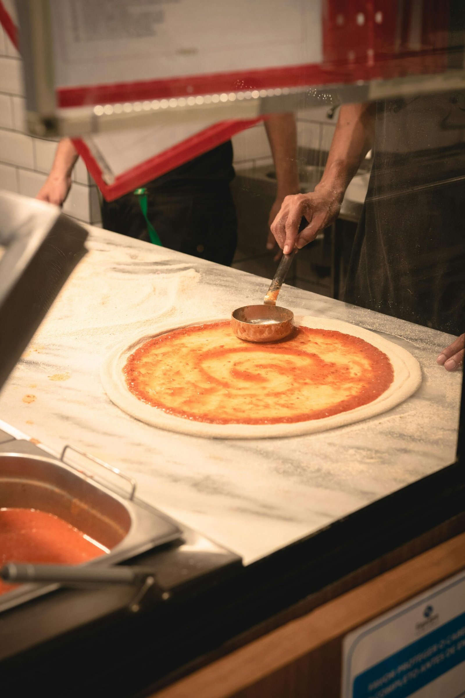 Authentic Italian pizza preparation with fresh tomato sauce on dough in a Brazilian kitchen.