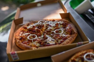 Close-up of a freshly baked pizza with toppings in a cardboard box, mouthwatering and ready to eat.